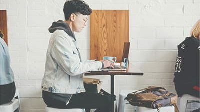 A person is sitting in the cafe and writing on a laptop